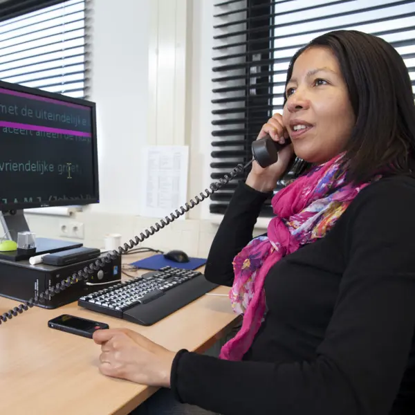 Vrouw zit achter de computer en is aan het bellen Vrouw zit achter de computer en is aan het bellen