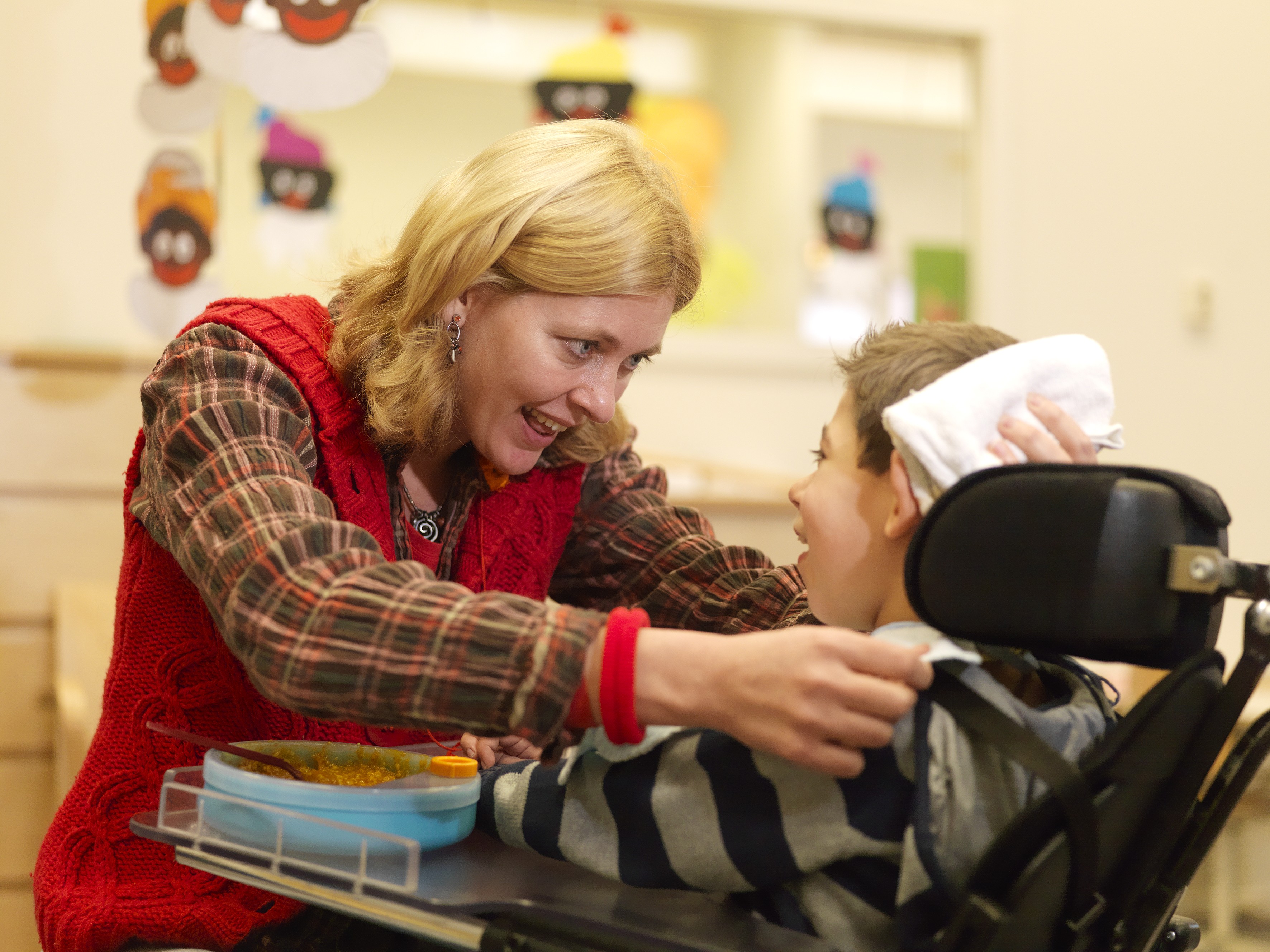 Begeleider heeft oogcontact met kind in rolstoel. 