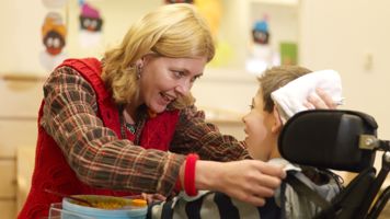 Begeleider heeft oogcontact met kind in rolstoel. Begeleider heeft oogcontact met kind in rolstoel.