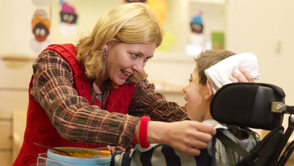 Begeleider heeft oogcontact met kind in rolstoel. Begeleider heeft oogcontact met kind in rolstoel.