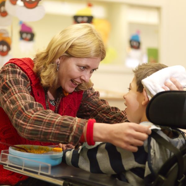 Begeleider heeft oogcontact met kind in rolstoel. Begeleider heeft oogcontact met kind in rolstoel.