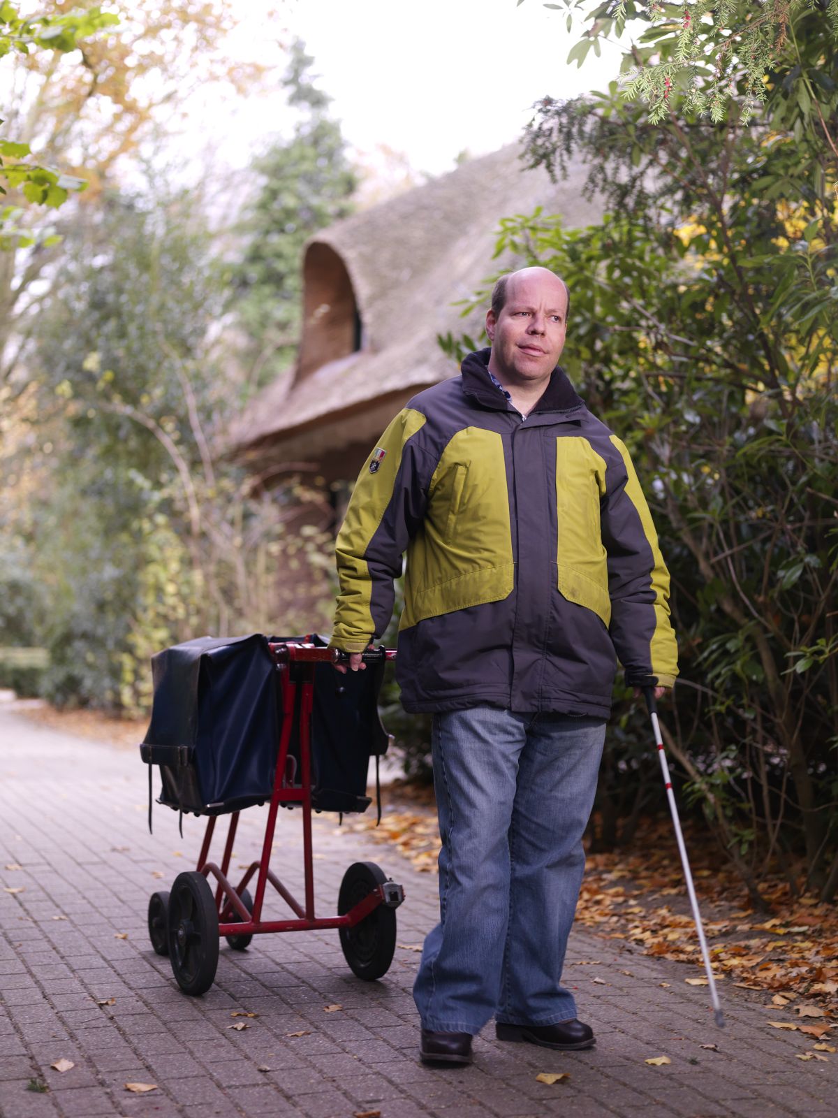 Cliënt brengt de post rond met een taststok in zijn hand en aan zijn andere hand een postwagentje