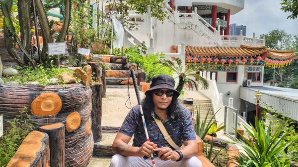 Emmanuel zit met zijn taststok op een trap bij een Thaise tempel Emmanuel zit met zijn taststok op een trap bij een Thaise tempel