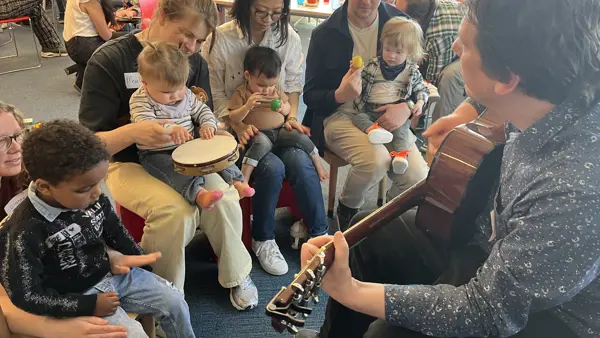 Ouders hebben jonge kinderen op schoot en de kinderen maken muziek met muziekinstrumentjes Ouders hebben jonge kinderen op schoot en de kinderen maken muziek met muziekinstrumentjes