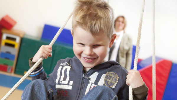 Een jongetje zit op een schommel. In de achtergrond zijn kleurrijke matten te zien. Een jongetje zit op een schommel. In de achtergrond zijn kleurrijke matten te zien.