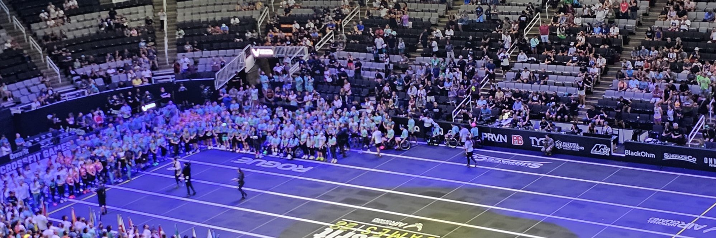 Foto van de sportzaal. De deelnemers staan in een U vorm om het midden van de zaal heen.