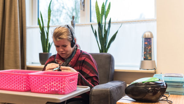 Cliënt zit in stoel en luister muziek met een koptelefoon Cliënt zit in stoel en luister muziek met een koptelefoon