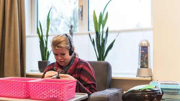 Cliënt zit in stoel en luister muziek met een koptelefoon Cliënt zit in stoel en luister muziek met een koptelefoon