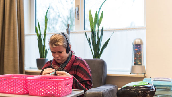 Cliënt zit in stoel en luister muziek met een koptelefoon Cliënt zit in stoel en luister muziek met een koptelefoon