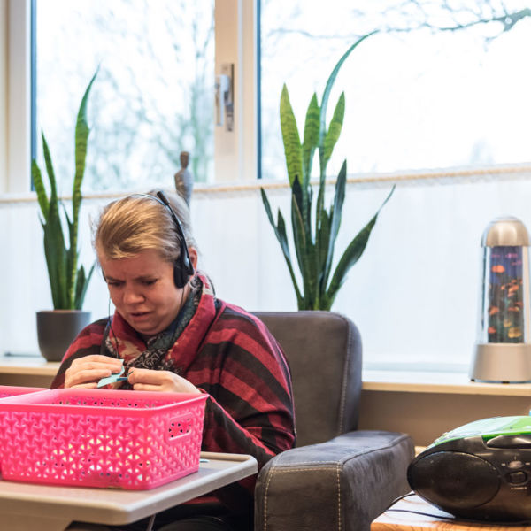 Cliënt zit in stoel en luister muziek met een koptelefoon Cliënt zit in stoel en luister muziek met een koptelefoon