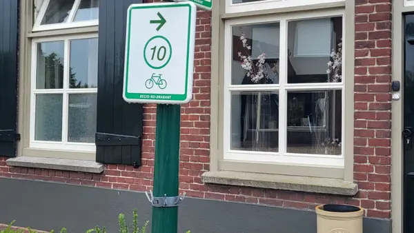 Een gebouw is te zien op de achtergrond. Op de voorgrond is een lantaarnpaal met een blauw straatnaambordje met "dorpstraat" erop. Op de paal zijn ook twee groen/witte bordjes van fietsroutes te zien. De bovenste wijst naar links en heeft het nummer 67, de onderste wijst naar rechts en heeft het nummer 10. Een gebouw is te zien op de achtergrond. Op de voorgrond is een lantaarnpaal met een blauw straatnaambordje met "dorpstraat" erop. Op de paal zijn ook twee groen/witte bordjes van fietsroutes te zien. De bovenste wijst naar links en heeft het nummer 67, de onderste wijst naar rechts en heeft het nummer 10.