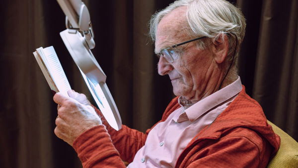 Man met visuele beperking leest met speciale leeslamp Man met visuele beperking leest met speciale leeslamp