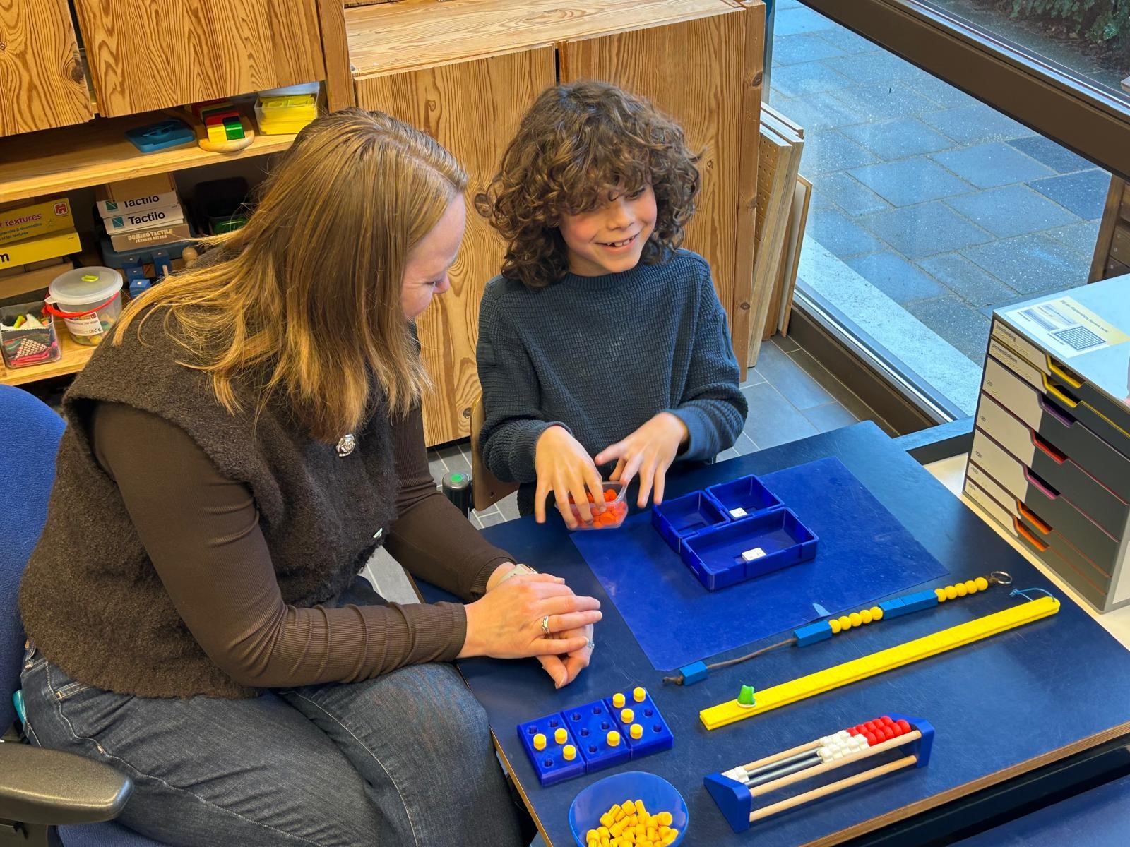 Jonah is samen met een begeleider aan het werk met de braille Rekenbox.
