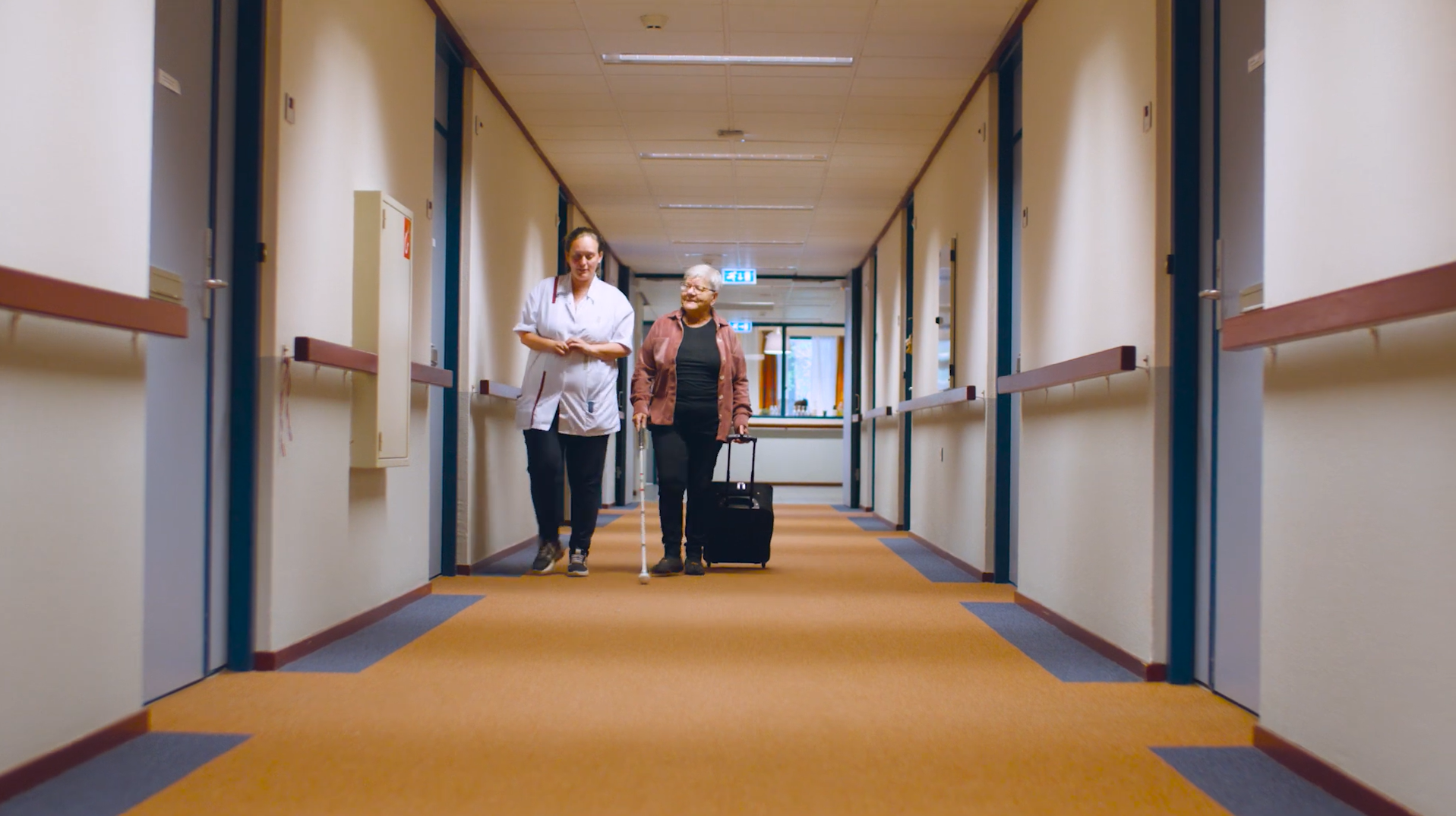 Cliënt met een taststok en een medewerker lopen samen door een hal van De Vlasborch