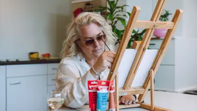 Een blonde vrouw zit aan een tafel. Ze is aan het schilderen. Een blonde vrouw zit aan een tafel. Ze is aan het schilderen.