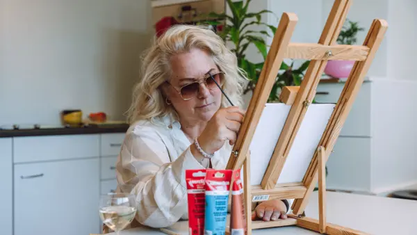 Een blonde vrouw zit aan een tafel. Ze is aan het schilderen. Een blonde vrouw zit aan een tafel. Ze is aan het schilderen.