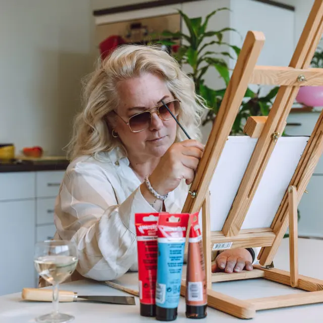 Een blonde vrouw zit aan een tafel. Ze is aan het schilderen. Een blonde vrouw zit aan een tafel. Ze is aan het schilderen.