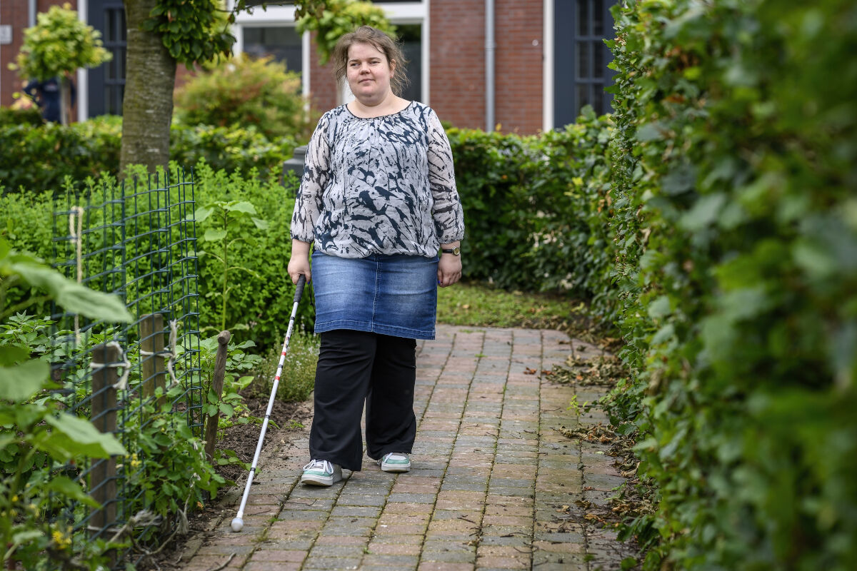 Dame met taststok loopt buiten op een stoepje bij Visio Wonen & Dagbesteding Stramproy