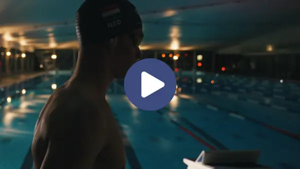 Rogier Dorsman loopt met een badmuts op naast een amper verlicht zwembad. Op de afbeelding staat een playbutton. Rogier Dorsman loopt met een badmuts op naast een amper verlicht zwembad. Op de afbeelding staat een playbutton.