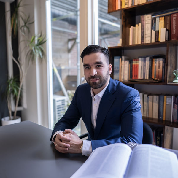 Foto van Faruk, hij zit aan een bureau in een kantoor met een blauw pak aan. Foto van Faruk, hij zit aan een bureau in een kantoor met een blauw pak aan.