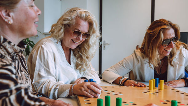 Drie vrouwen spelen samen een tactiele versie van Mens erger je niet. Drie vrouwen spelen samen een tactiele versie van Mens erger je niet.