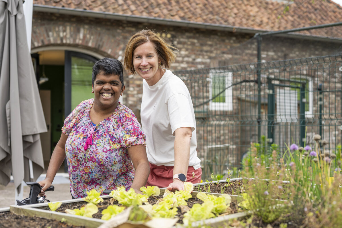 Cliënt en medewerker van Visio poseren glimlachend bij een moestuin