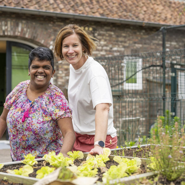 Cliënt en medewerker van Visio poseren glimlachend bij een moestuin Cliënt en medewerker van Visio poseren glimlachend bij een moestuin