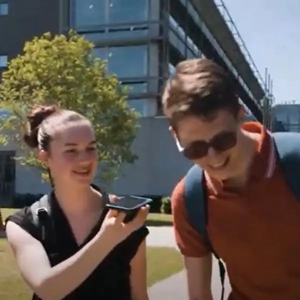 Drie leerlingen lopen samen. Het middelste meisje laat de jongen aan haar linkerkant iets horen met haar telefoon. Drie leerlingen lopen samen. Het middelste meisje laat de jongen aan haar linkerkant iets horen met haar telefoon.