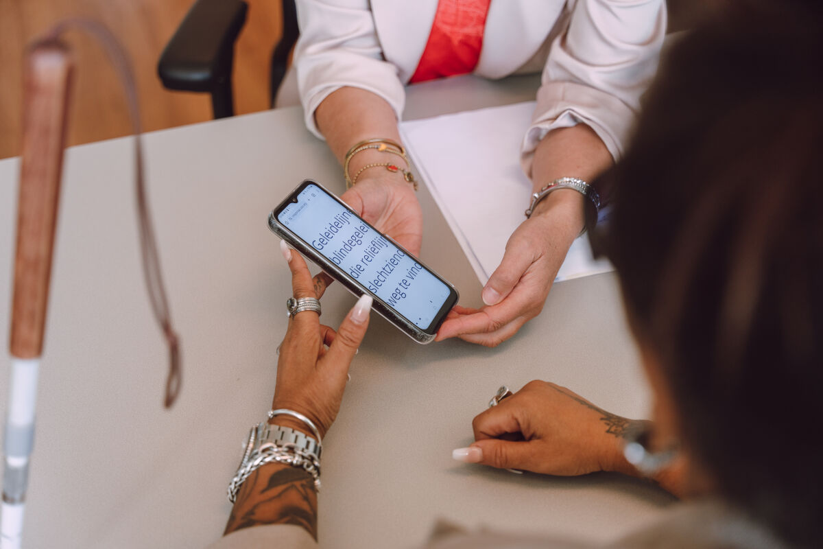 Twee paar handen houden een telefoon vast. Er staat vergrote tekst in beeld. 