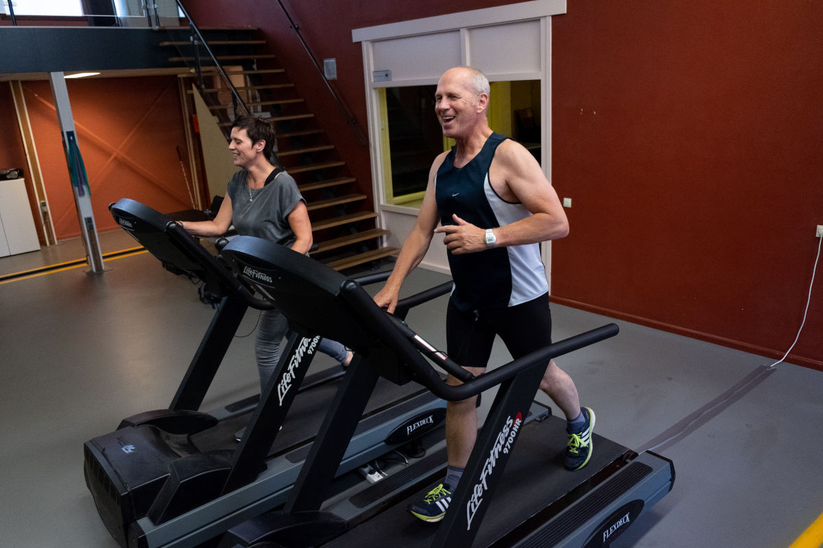 Een man en een vrouw staan beide op een loopband. 