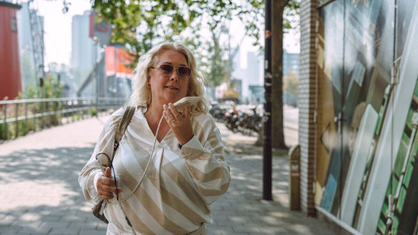 Vrouw met taststok telefoneert buiten. Vrouw met taststok telefoneert buiten.
