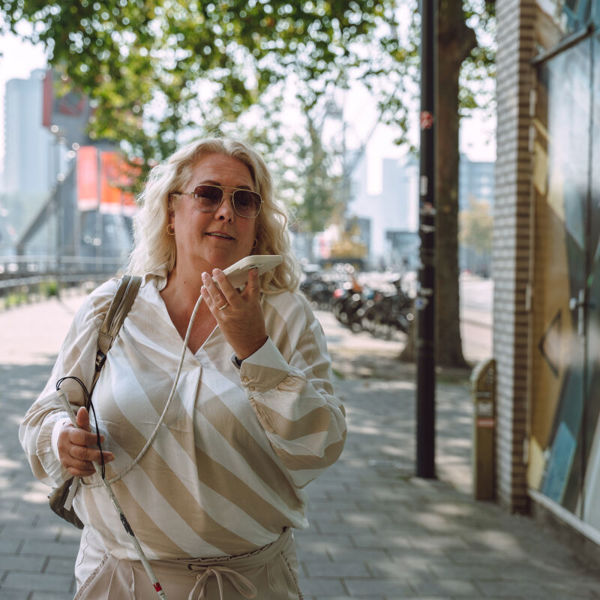 Vrouw met taststok telefoneert buiten. Vrouw met taststok telefoneert buiten.
