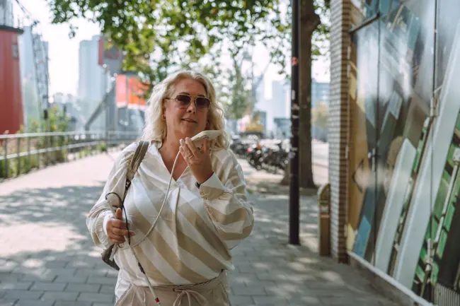 Vrouw met taststok telefoneert buiten. Vrouw met taststok telefoneert buiten.