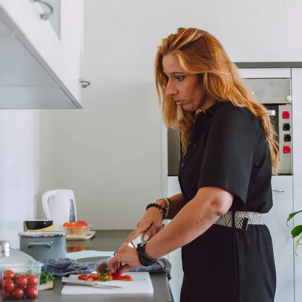 Een vrouw is in de keuken tomaten aan het snijden. Ze leest het recept op een iPad, waarop de tekst vergroot is. Een vrouw is in de keuken tomaten aan het snijden. Ze leest het recept op een iPad, waarop de tekst vergroot is.