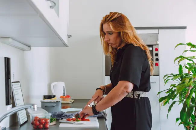 Een vrouw is in de keuken tomaten aan het snijden. Ze leest het recept op een iPad, waarop de tekst vergroot is. Een vrouw is in de keuken tomaten aan het snijden. Ze leest het recept op een iPad, waarop de tekst vergroot is.