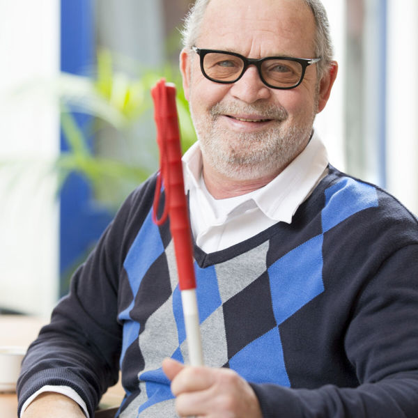 Oudere man met glaucoom glimlacht zittend met een taststok in zijn hand Oudere man met glaucoom glimlacht zittend met een taststok in zijn hand