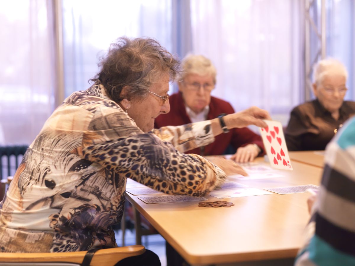 Een groepje ouderen speelt een kaartspel. De kaarten zijn extra groot met grote opdruk. 