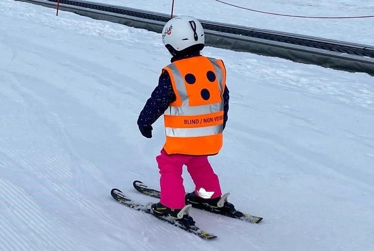 U ziet het meisje skiën met het ski hesje voor blinde en slechtziende mensen