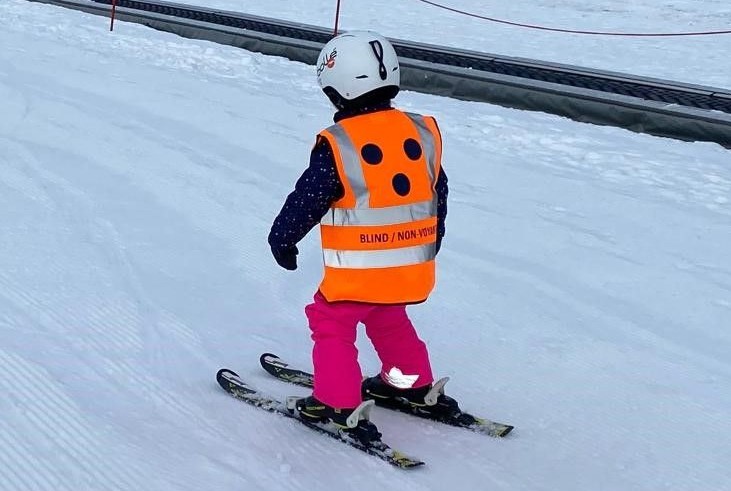 U ziet het meisje skiën met het oranje ski hesje voor blinde en slechtziende mensen U ziet het meisje skiën met het ski hesje voor blinde en slechtziende mensen