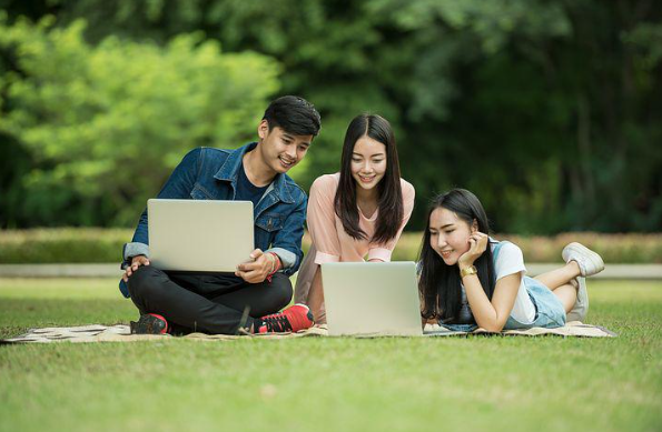 Twee vrouwen en een man zitten met hun computers op het grasveld