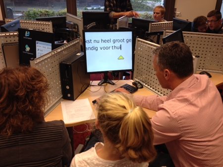 Foto van kind en ouders achter een computer met vergrote tekst. Foto van kind en ouders achter een computer met vergrote tekst.