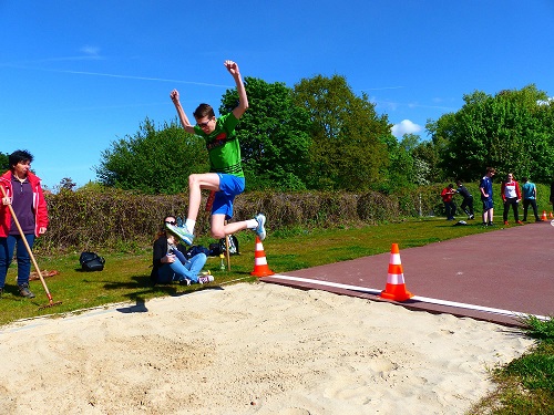 Jongen met bril springt ver op een vlak met zand