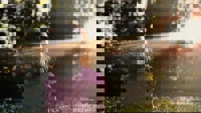 Een meisje zit in het bos op het gras. De zon schijnt door de bomen heen, ze kijkt richting het licht. Een meisje zit in het bos op het gras. De zon schijnt door de bomen heen, ze kijkt richting het licht.